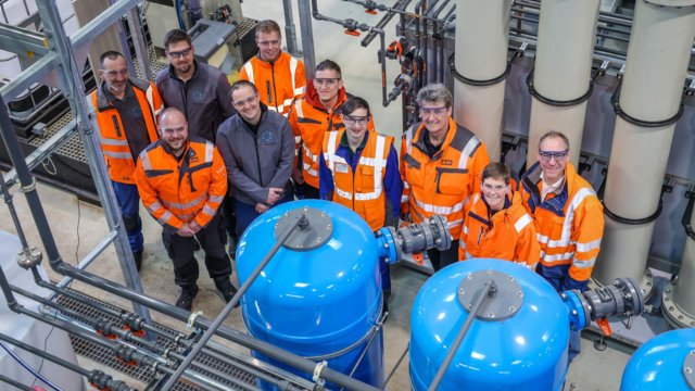 Die verantwortlichen Akteurinnen und Akteure zwischen den Ionenaustauscher-Stufen der Rückgewinnungsanlage: (v.L.n.r.) Carsten Bräuer, Dr. Dennis Blöhse, Fabian Rovers (alle EG/PhosRec), Christoph Thiel (PTC), Willi Markwart (EG/PhosRec), Andre Bends, Dr. Reinhard Lohmeier, Jürgen Waller (alle PTC), Dr. Yvonne Schneider (RV/PhosRec), Prof. Torsten Frehmann (EG/PhosRec) [Quelle: ELGV / Rupert Oberhäuser]